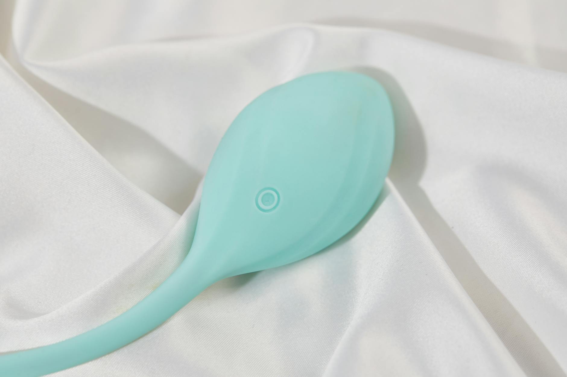 A teal vibrator on soft white silk fabric, intimate and modern