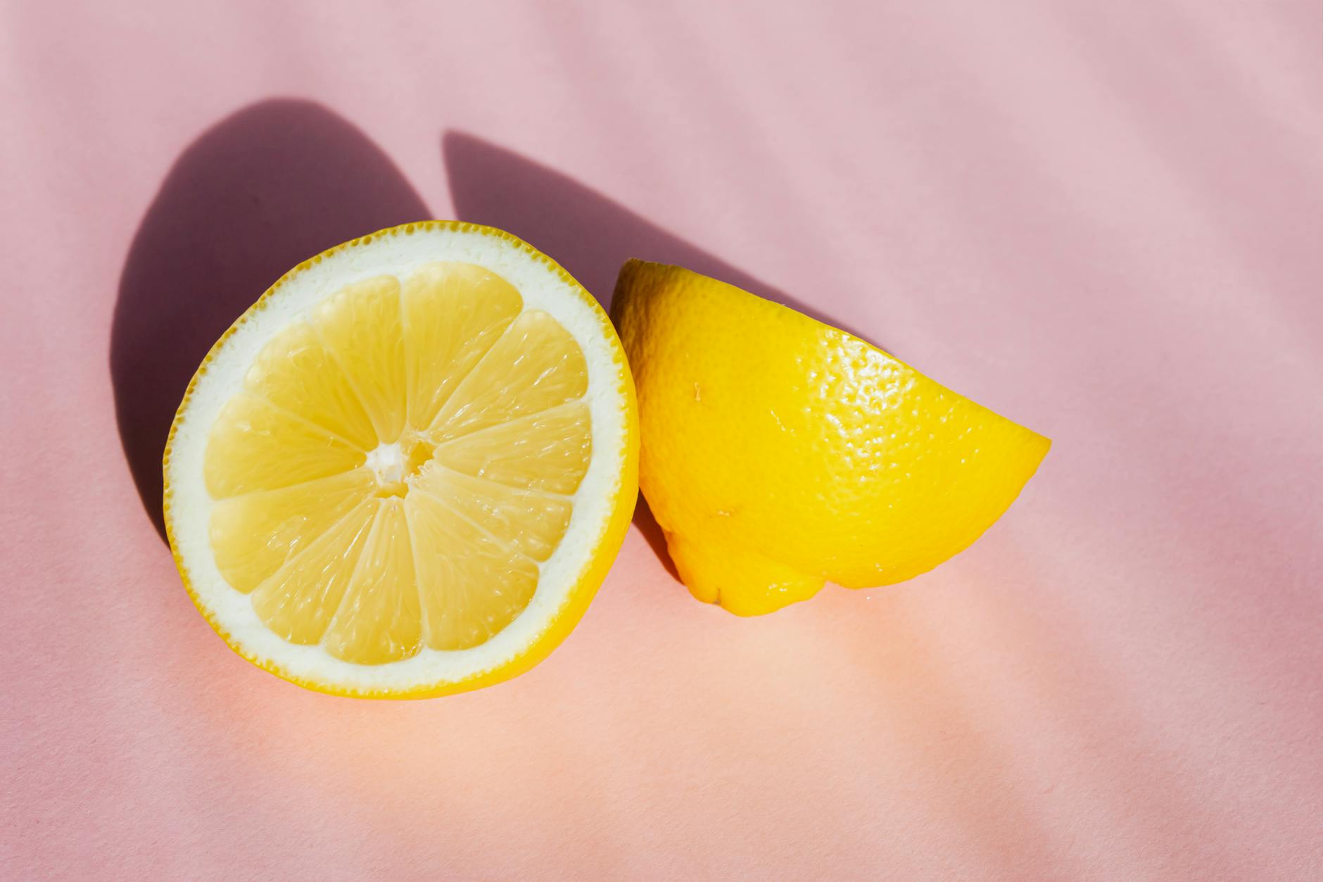 Fresh lemon halves on a pink background in natural sunlight, symbolizing delicate and bright sensations
