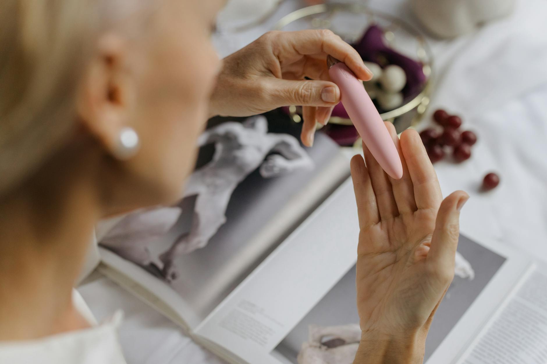 Close-up of a hand holding a vibrator against art books, emphasizing intimacy and personal wellness.