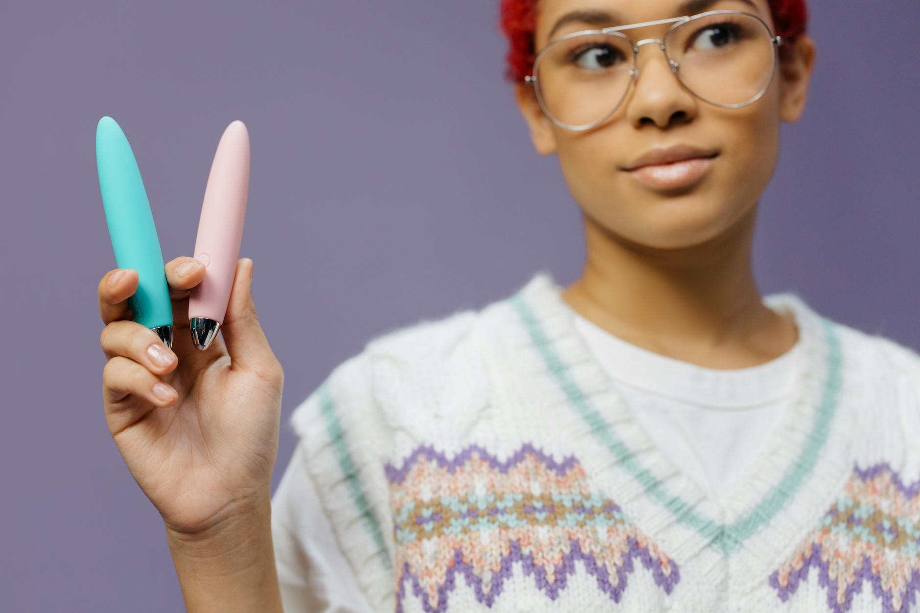 Woman holding colorful vibrators against a purple background, exploring pleasure and sensation