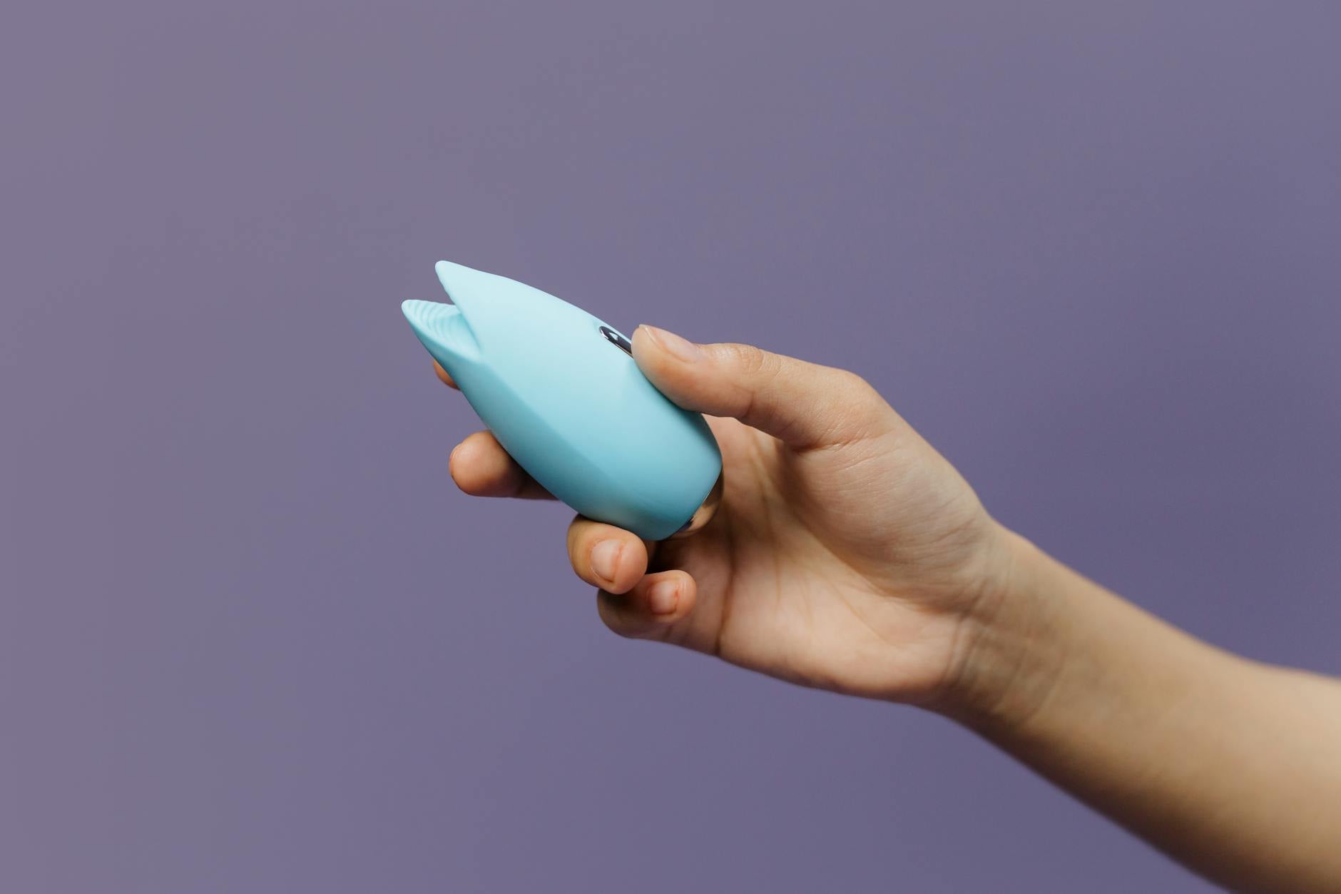 A hand holding a blue silicone vibrator against a purple background, symbolizing self-love and intimate exploration.
