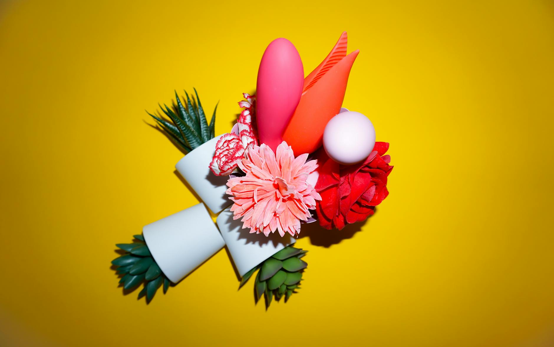 A hand reaching over a variety of colorful sex toys arranged on a table.