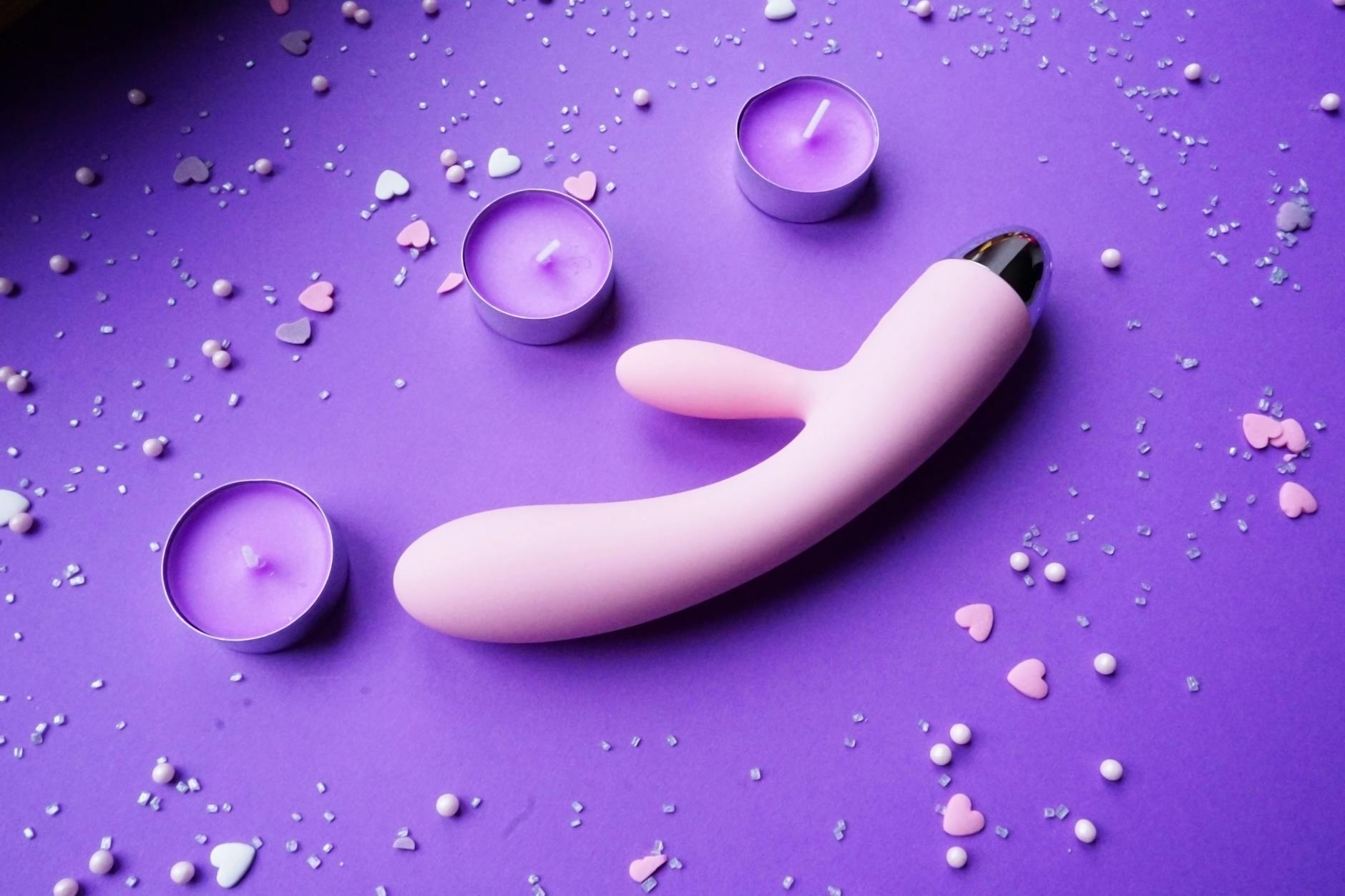 Pink vibrator on purple background with heart confetti and candles, symbolizing intimate couple time